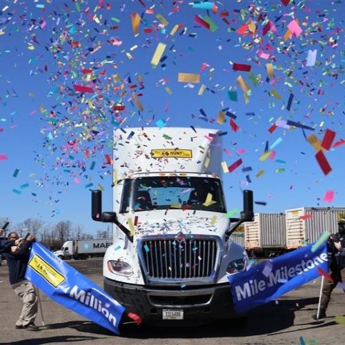 Rainbow-colored confetti flying around a J.B. Hunt truck driving through a blue banner with the words 'J.B. Hunt Million Mile Milestone' on it.