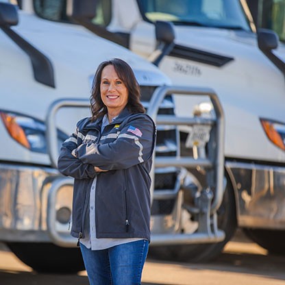 Confident woman standing with arms crossed in front of J.B. Hunt trucks, highlighting the company’s transportation services