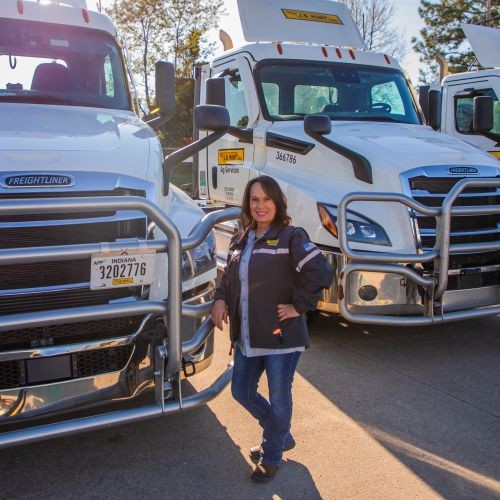 J.B. Hunt driver, Melinda, is smiling proudly in front of three J.B. Hunt Ag Services trucks.