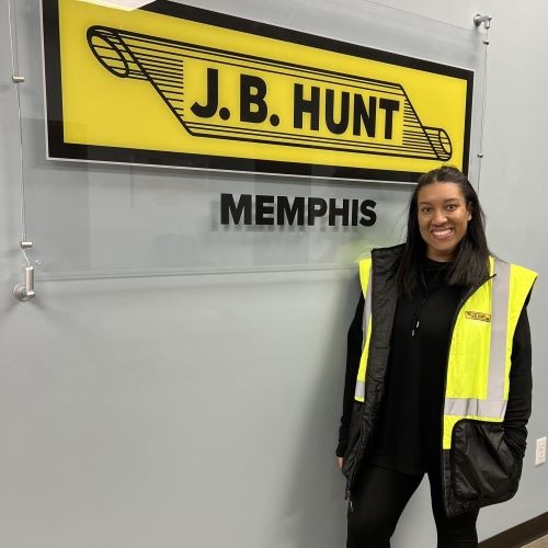 Group photo of the J.B. Hunt Northeast region's drivers standing in front of a blue and yellow balloon arch holding trophies and smiling signifying a win! twenty drivers, both men and women, are wearing matching blue J.B. Hunt polos on a sunny day