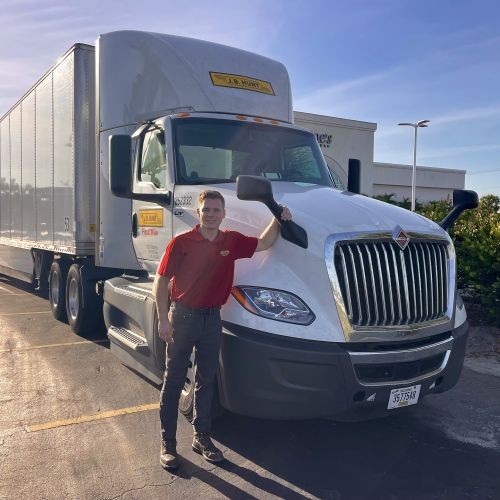 J.B. Hunt driver standing in front of J.B. Hunt truck while holding onto a rearview mirror.