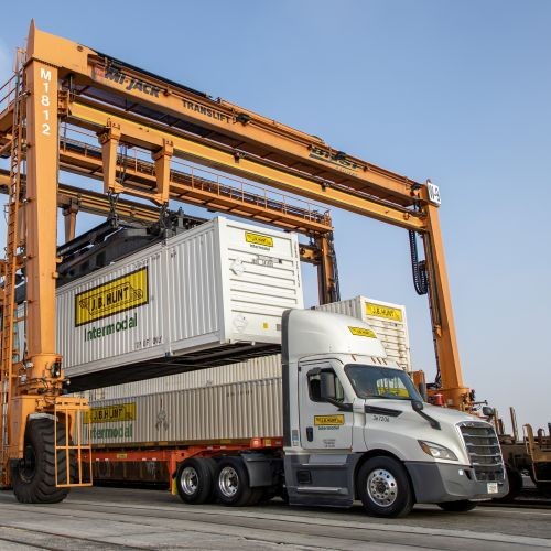 J.B. Hunt Intermodal truck underneath an orange translift receiving a J.B. Hunt Intermodal container.