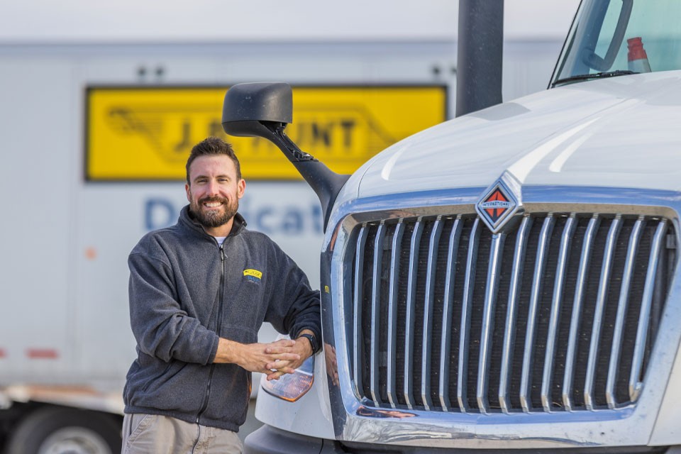 A J.B. Hunt Dedicated truck driver standing in front of their truck smiling.