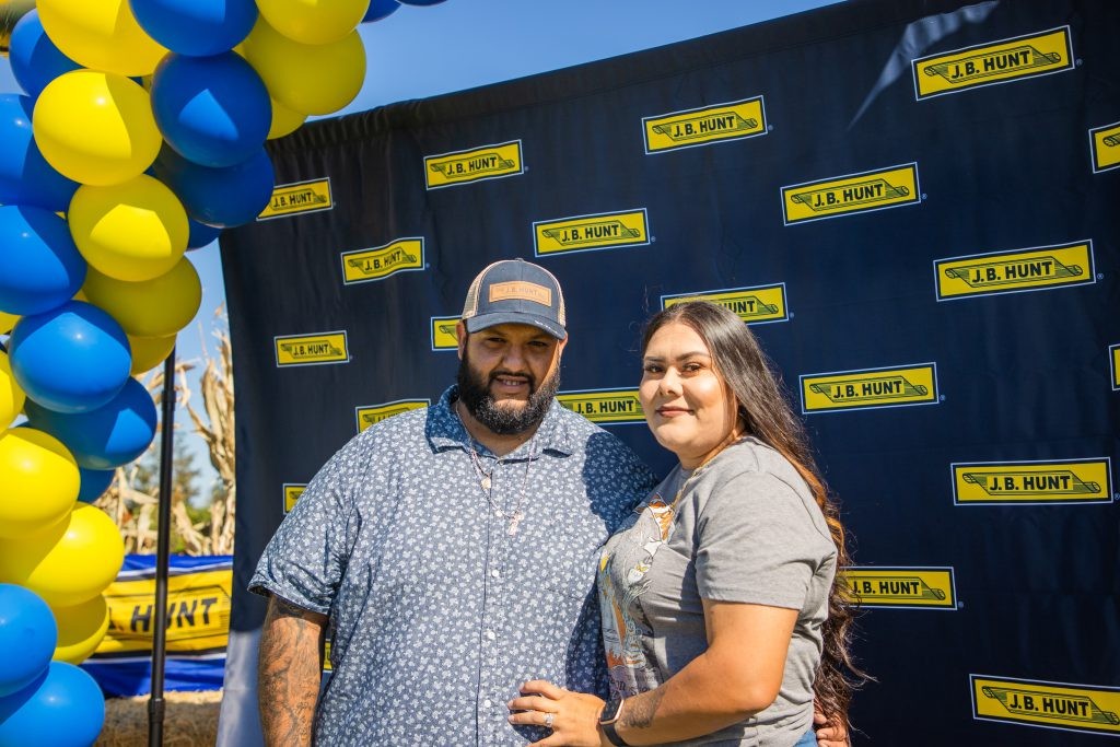 A J.B. Hunt driver posing for a photo with his wife in front of a J.B. Hunt banner.
