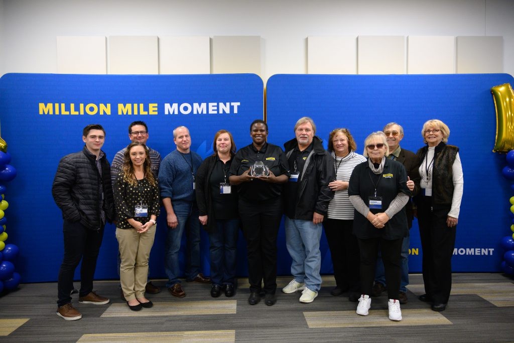 A group of J.B. Hunt employees stand in front of a million mile moment background while one member holds an  award