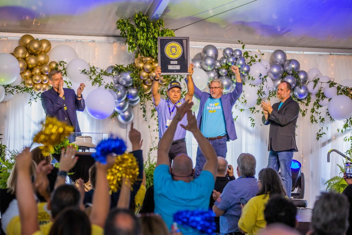 J.B. Hunt 5 million mile safe driver, Tony, holds up his framed award on stage while a crowd cheers.