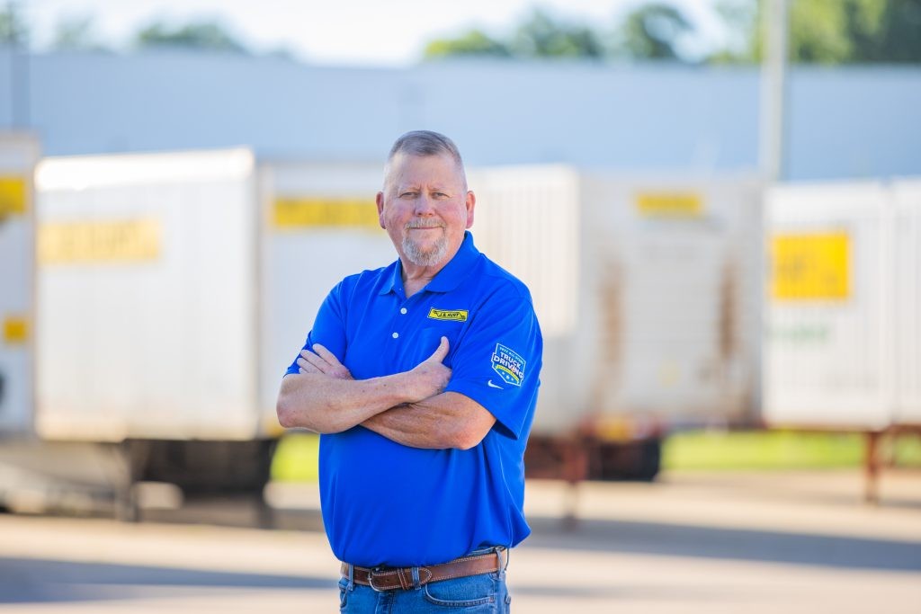 J.B. Hunt driver James stands and smiles at a camera.