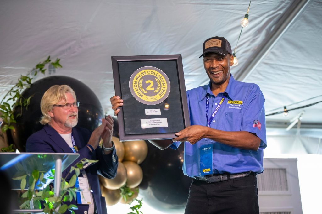 J.B. Hunt two-million-mile safe driver accepts award on stage with Greer Woodruff applauding him in the background.
