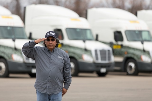 J.B. Hunt driver veteran, Louis, standing in front of a fleet of trucks and saluting the camera.