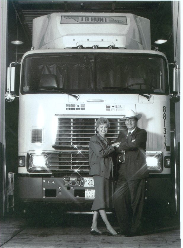 Mr. and Mrs. Hunt pose for a photo in front of a cabover truck, holding hands.