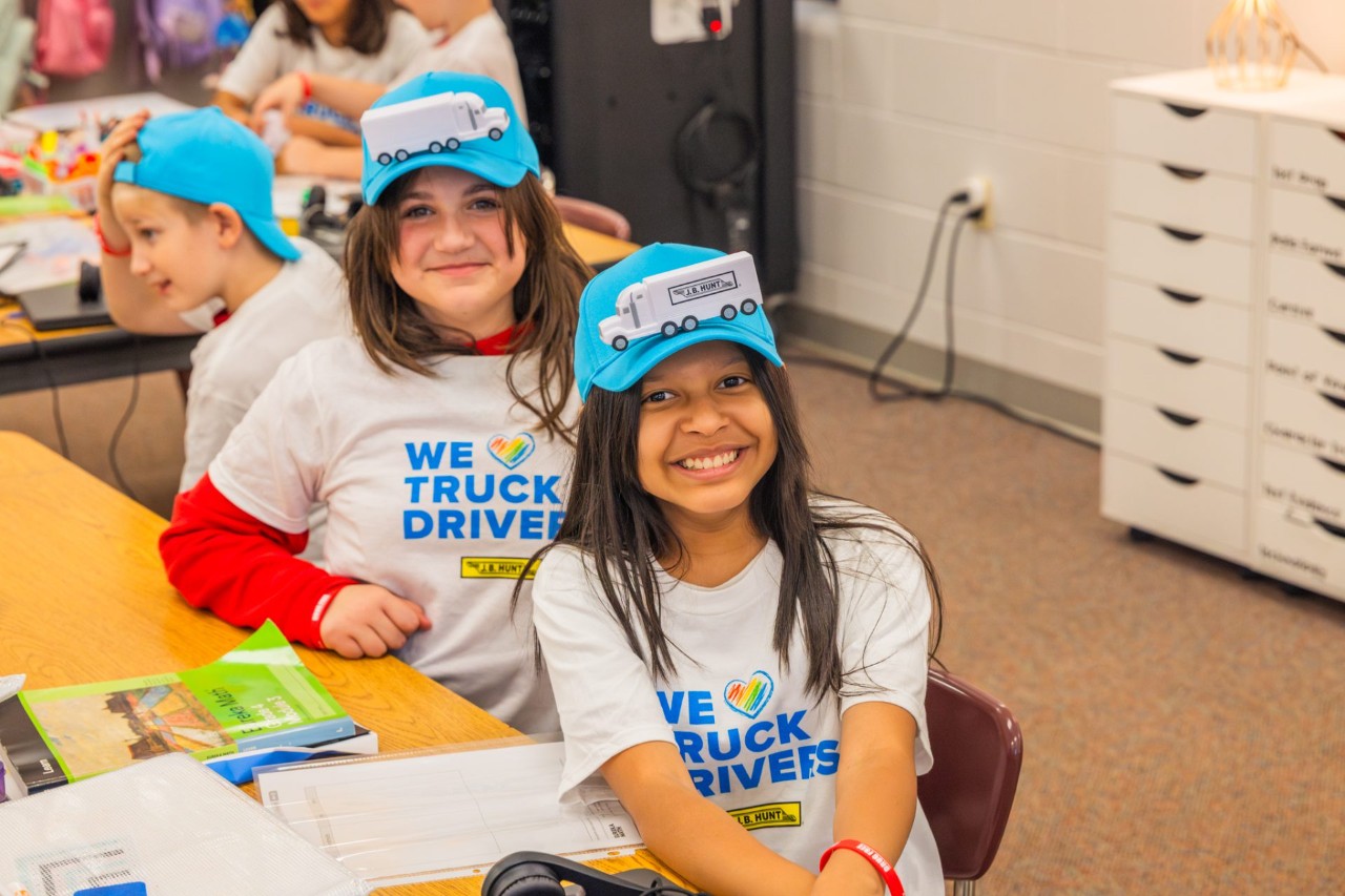 Students of an Adopt a Class classroom smile at the camera in J.B. Hunt T-shirts and hats.