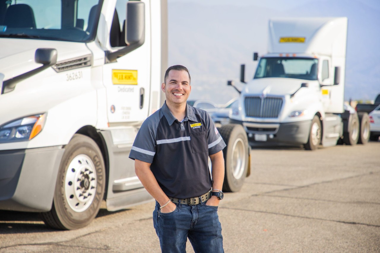 J.B. Hunt driver standing in front of J.B. Hunt Dedicated Contract Services trucks and smiling