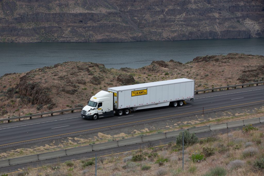 J.B. Hunt semi truck and trailer on a highway beside a lake.