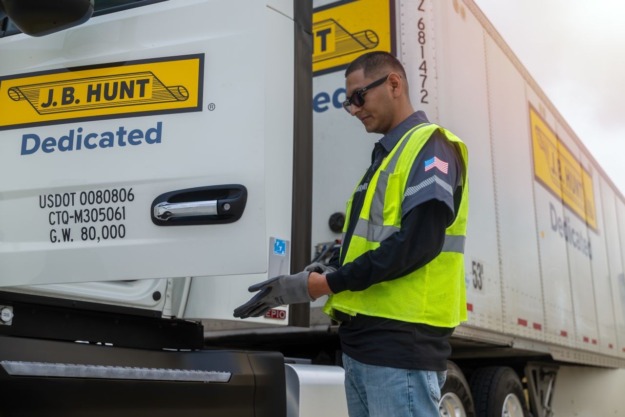 Driver wearing safety gear opening the door of a J.B. Hunt Dedicated truck, illustrating professional DCS operations and modern fleet equipment.