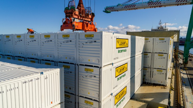 Refrigerated Shipping Containers Being Loaded at a Port Stacked white refrigerated shipping containers with “Intermodal” branding being loaded onto a cargo vessel using an overhead crane at a busy port.