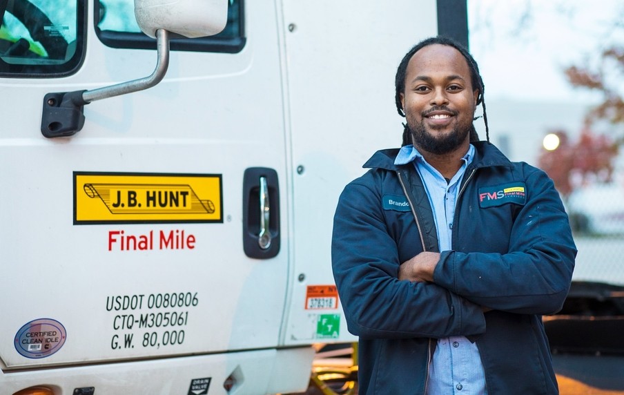 A J.B. Hunt final mile driving standing next to the door of a truck with arms crossed and smiling.