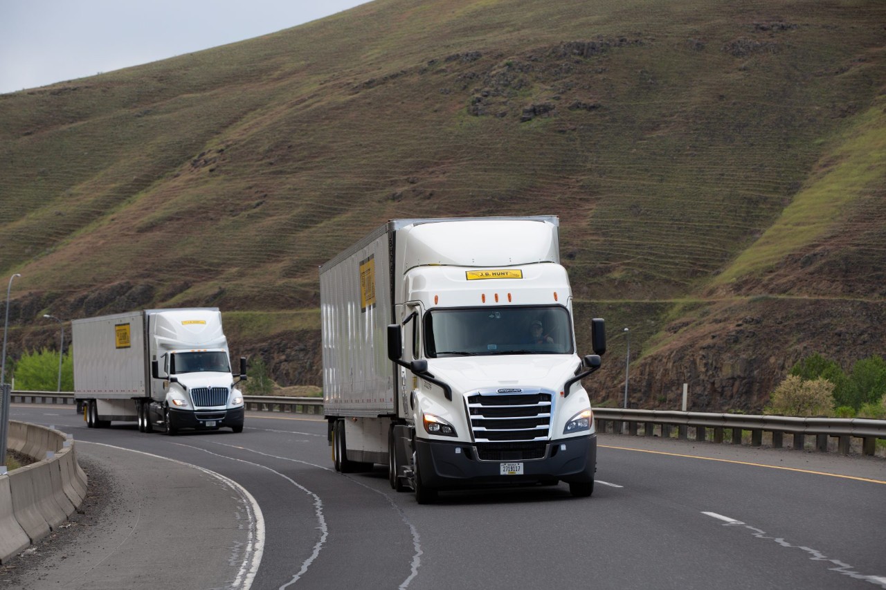 Two J.B. Hunt trucks driving around a bend on a highway.