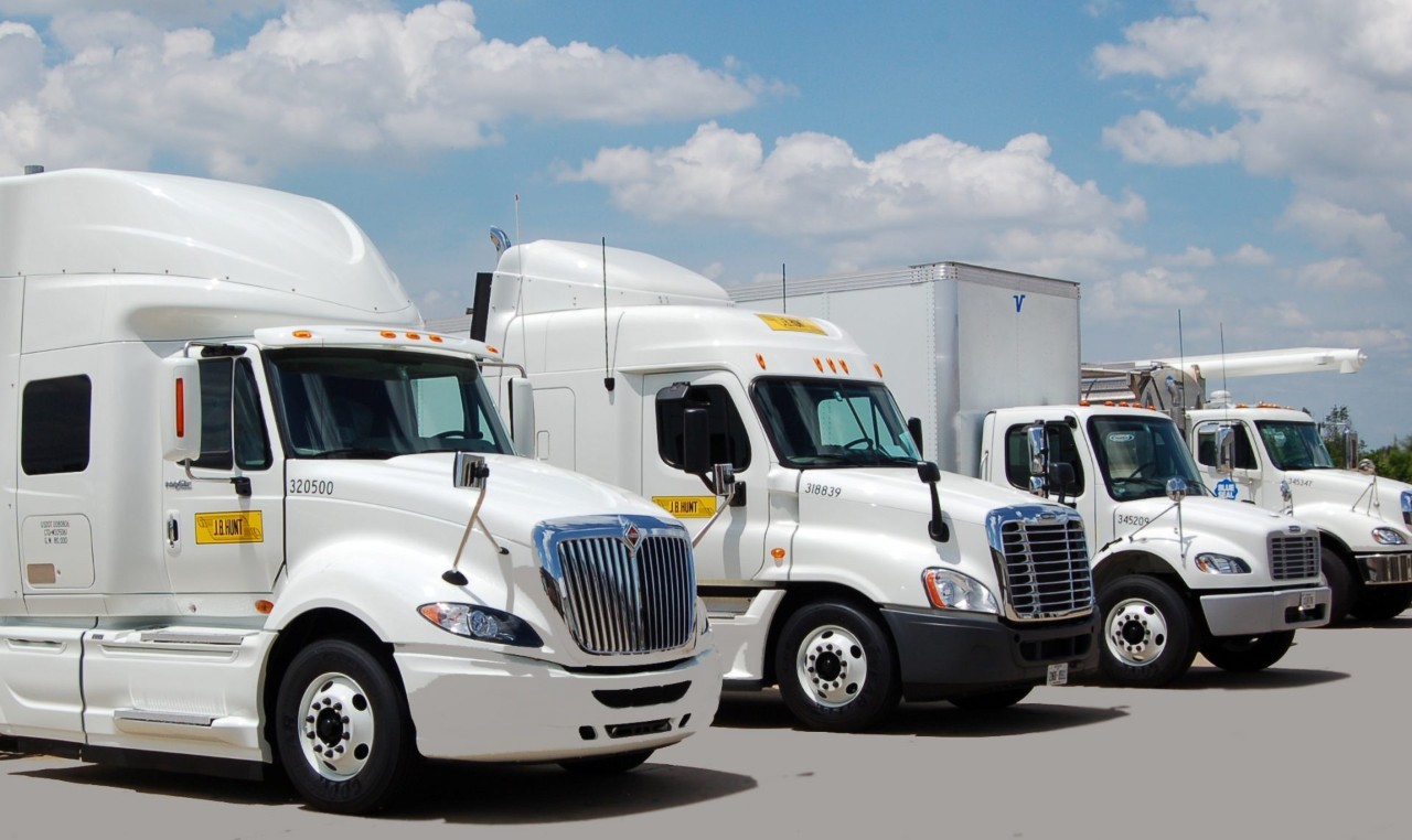 A line of different types J.B. Hunt branded trucks in a parking lot.