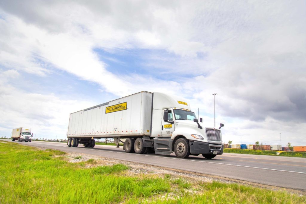 J.B. Hunt DCS day cab and trailer drive down a road.
