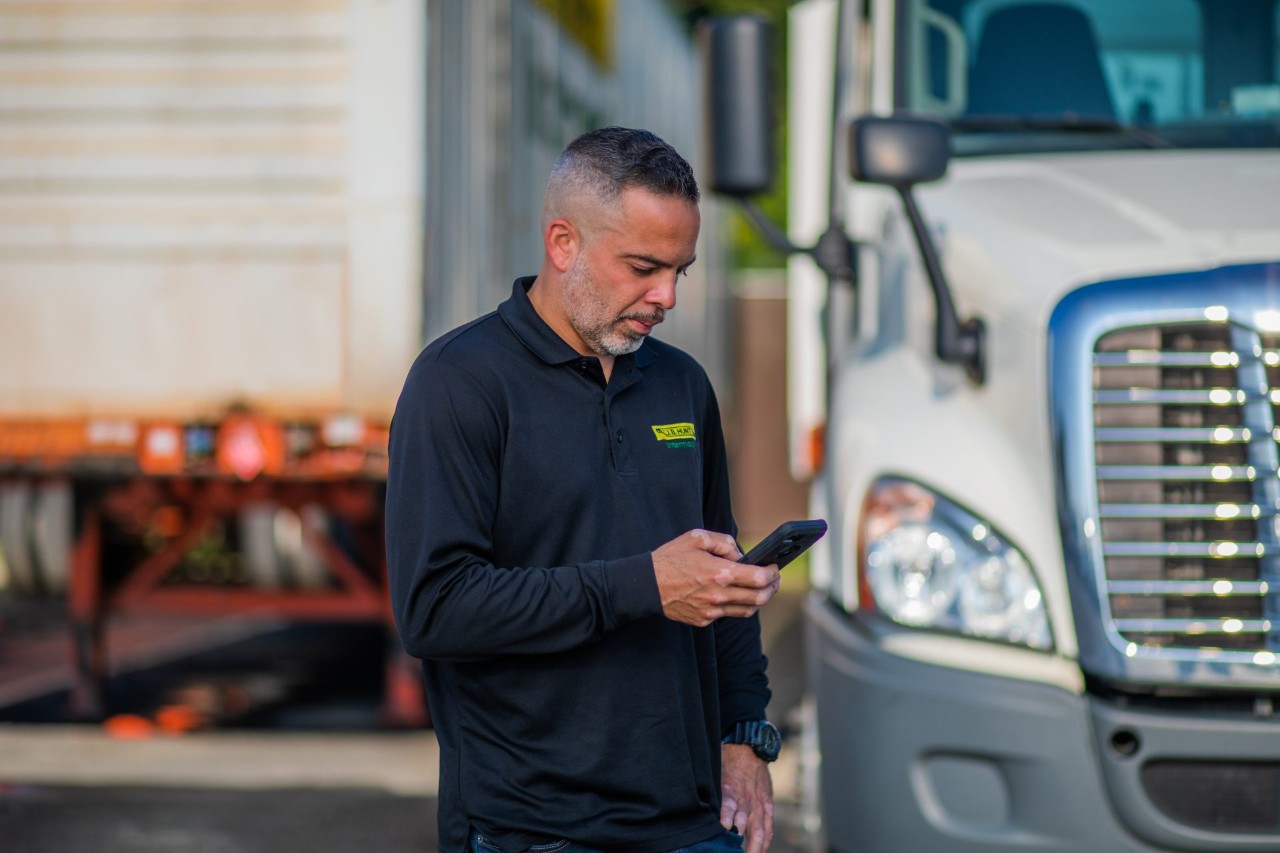 J.B. Hunt driver, Jose, checking the DRIVE App while standing in front of a truck.