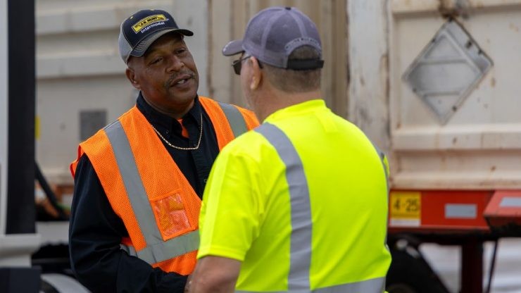 Two J.B. Hunt drivers in safety gear talk beside a trailer.