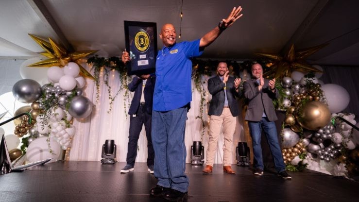 J.B. Hunt driver James holds his Million Mile Award on a stage and waves at a crowd.