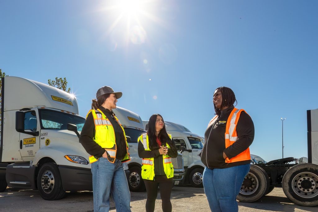 Three J.B. Hunt drivers standing in a truck yard.