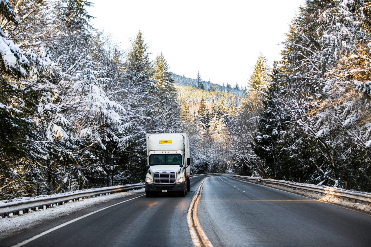 J.B. Hunt truck and trailer traveling down a snowy forest highway.