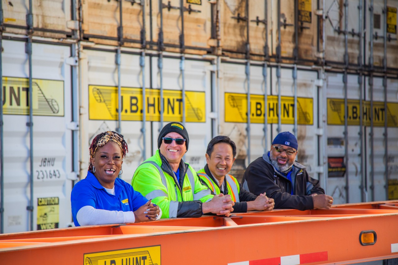 A group of J.B. Hunt employees with their arms relaxing on a rail as they smile at the camera.