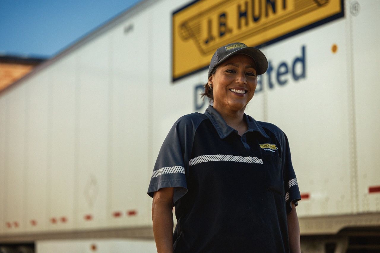 Uniformed transportation professional standing beside a J.B. Hunt dedicated fleet semi-trailer in an outdoor trucking yard setting.