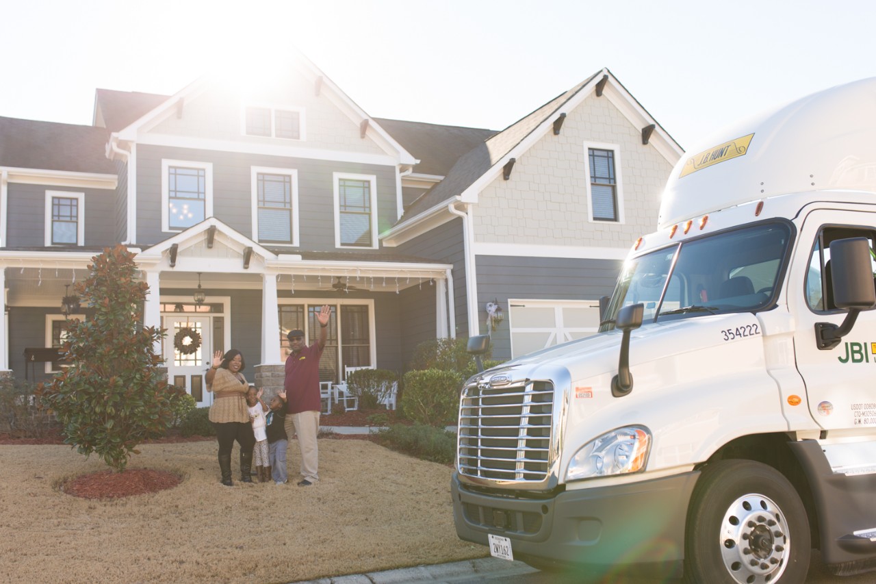 A J.B. Hunt driver and his family standing outside of their home waving at the camera.