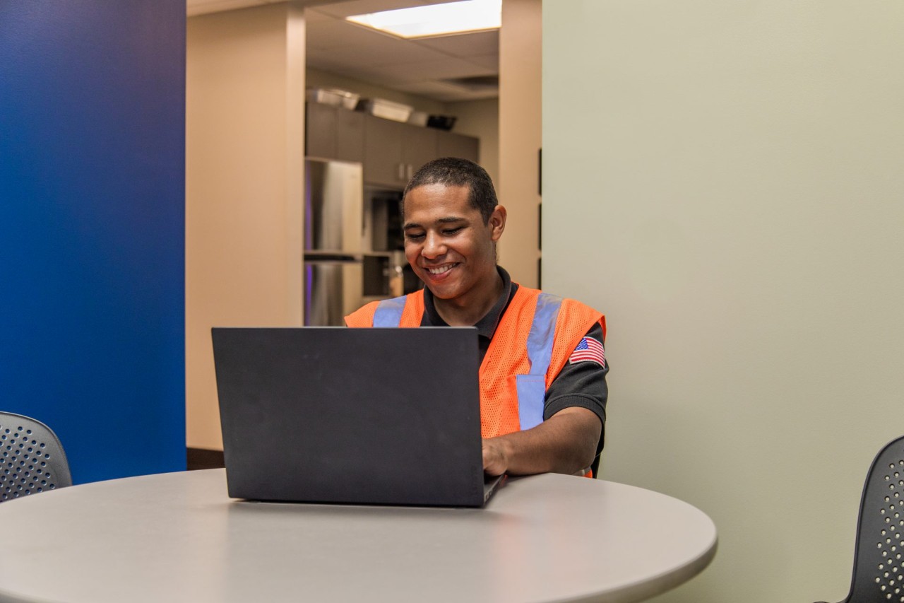A J.B. Hunt driver sitting in a break room working on a computer.