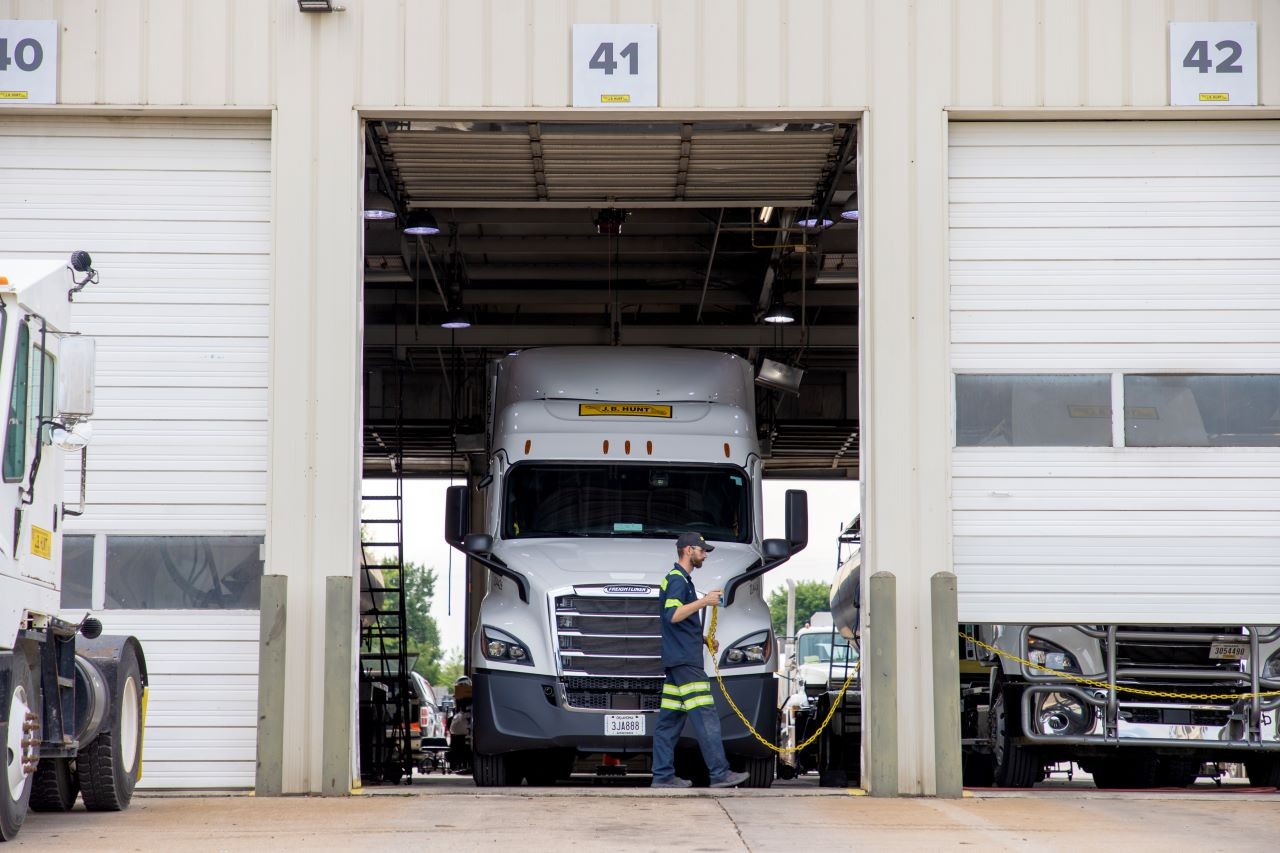 A J.B. Hunt maintenance technician walks in front of a J.B. Hunt day cab inside a maintenance shop.