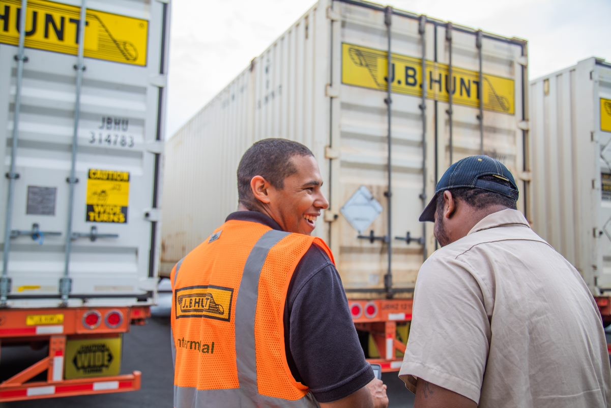 J.B. Hunt company drivers talking and laughing in front of J.B. Hunt trailers.