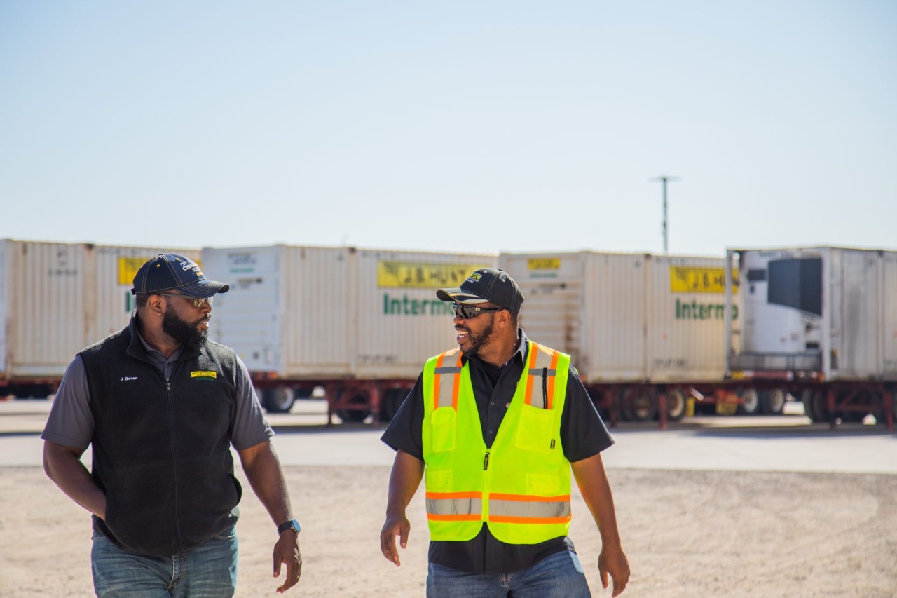 Two J.B. Hunt drivers walking and talking through an intermodal yard.