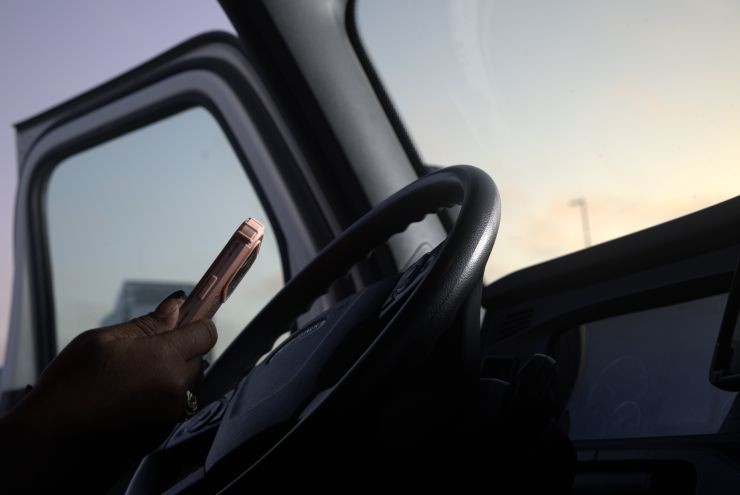 Close-up of a hand holding a smartphone inside a truck cab with steering wheel and dashboard visible.
