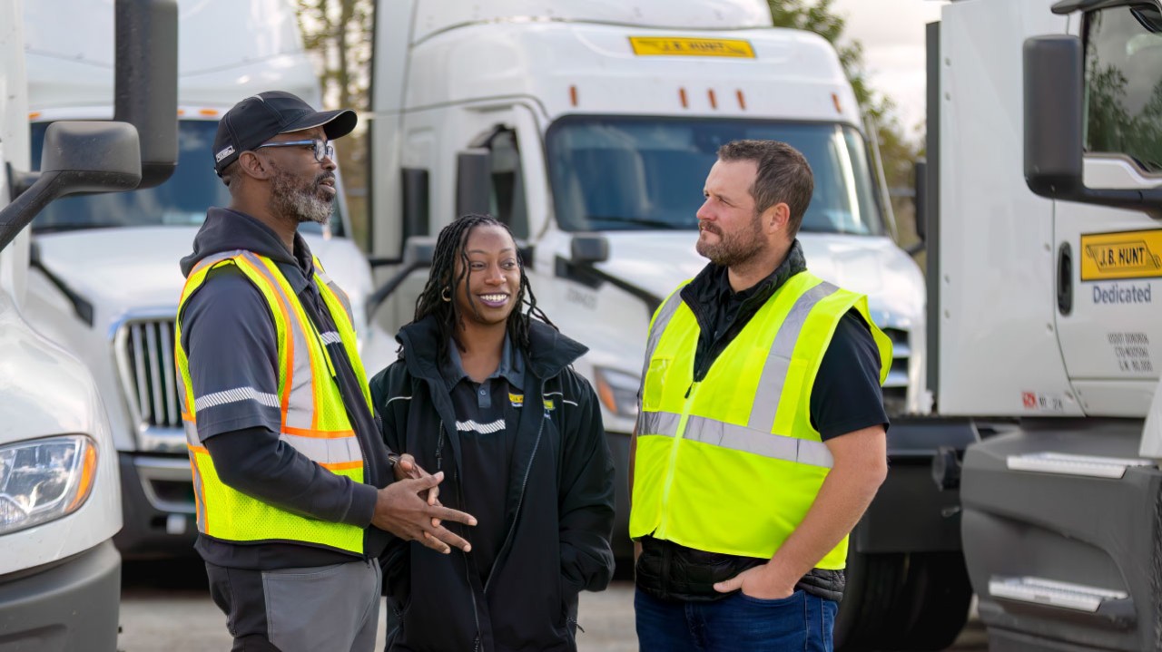 Three J.B. Hunt drivers standing and talking in a J.B. Hunt yard.