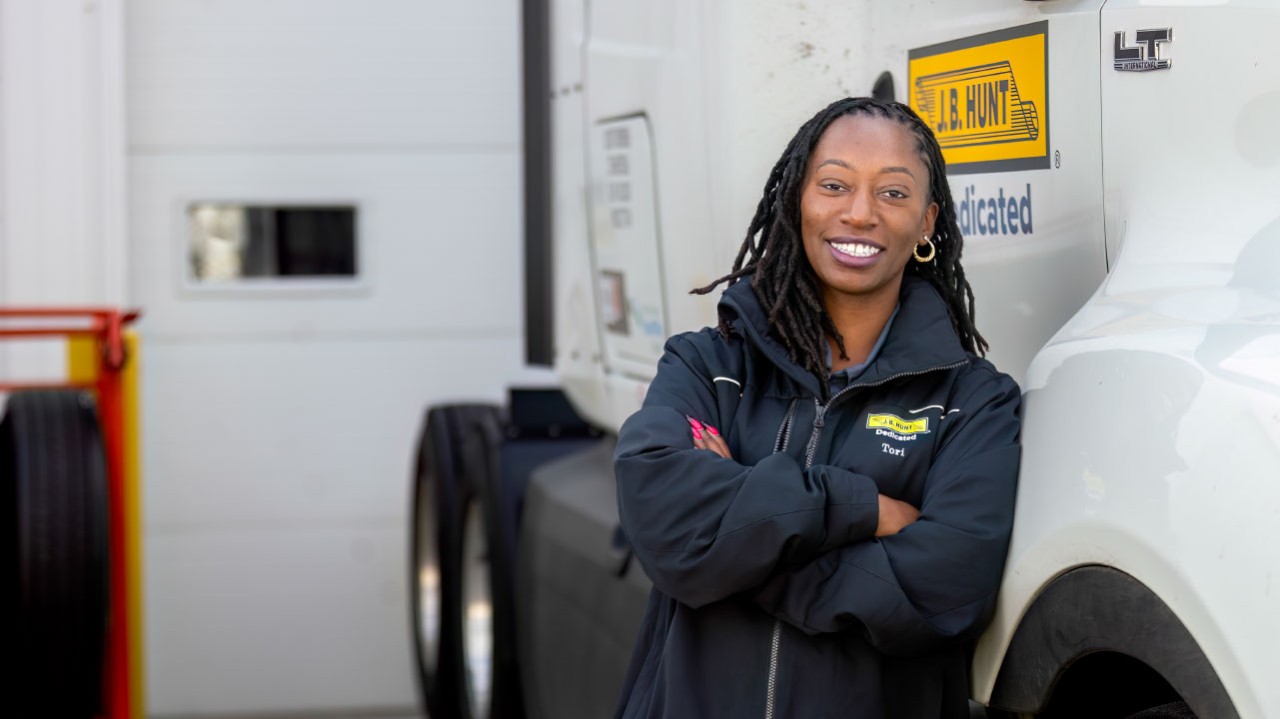 J.B. Hunt driver, Tori, leaning up against a J.B. Hunt truck with crossed arms and smiling at the camera.