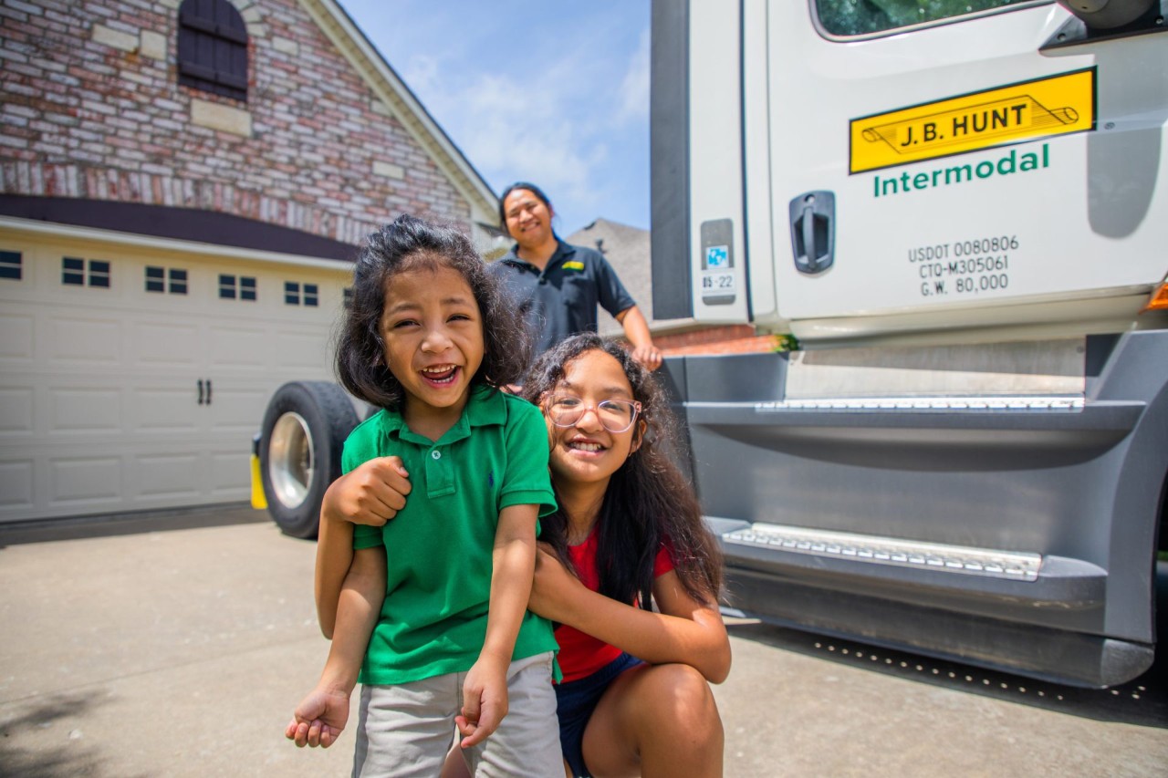 J.B. Hunt driver with his kids smiling at the camera while standing by an intermodal truck.
