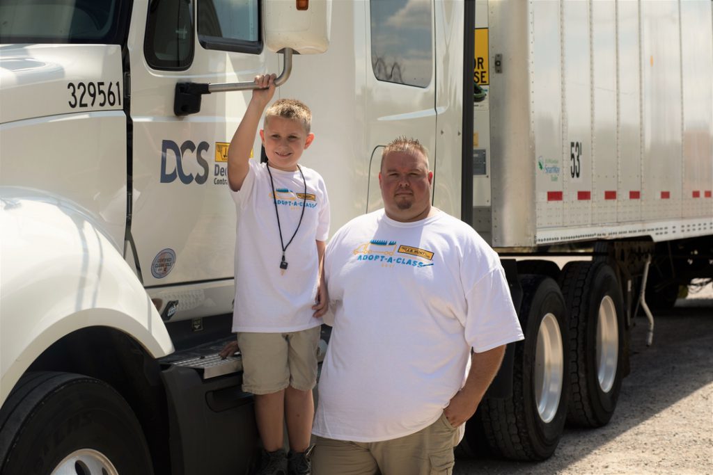 JB Hunt dedicated driver Robert stands next to truck with his son after Adopt-a-Class program donations are made. 