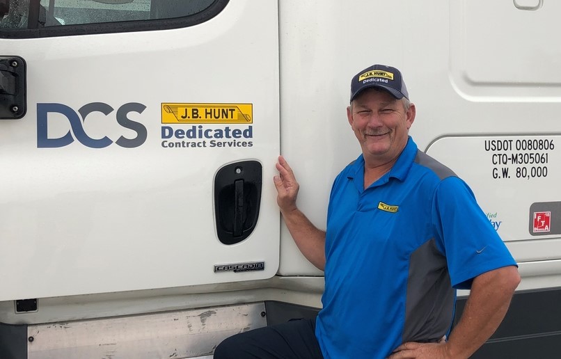 J.B. Hunt dedicated driver Darrell standing next to truck cab smiling. 