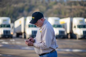 j.b. hunt driver working on their iphone standing in front of trucks