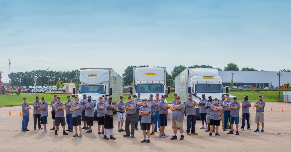 J.B. Hunt drivers standing in group with J.B. Hunt trucks in the background.