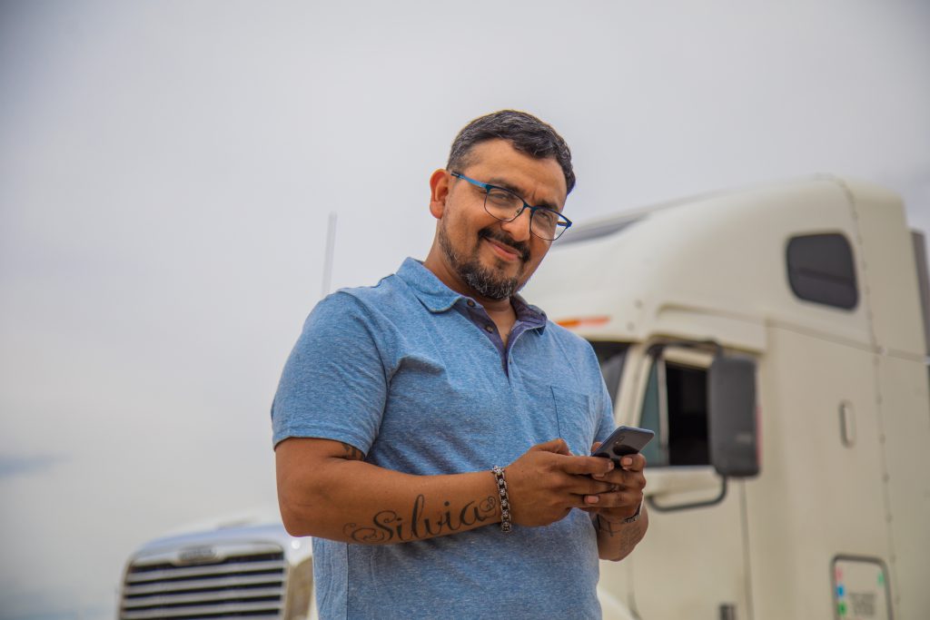 Tomas, and owner operator contracted with J.B. Hunt, stands in front of his truck and smiles.