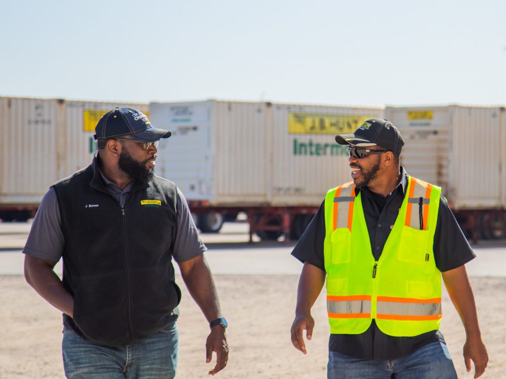Two truck drivers walking in an Intermodal yard talking to each other.