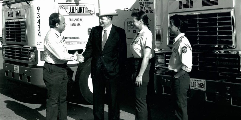 Mr. Hunt shakes hands with three J.B. Hunt drivers standing in front of two J.B. Hunt trucks.