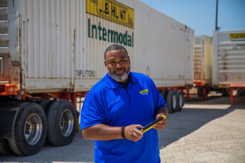J.B. Hunt driver trainer stands in front of an intermodal container and smiles.