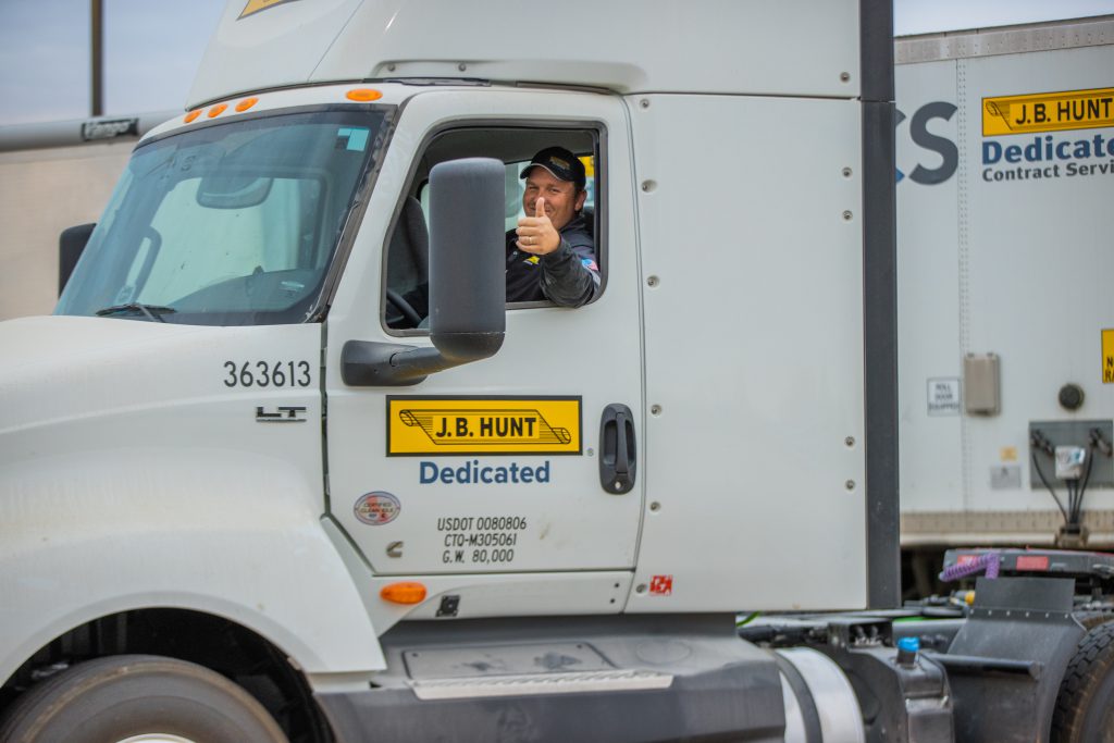 J.B. Hunt Dedicated driver gives a thumbs-up while sitting in a day cab.
