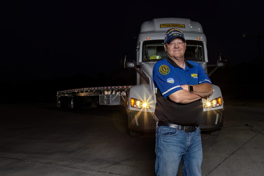 J.B. Hunt driver stands with arms crossed in front of a J.B. Hunt truck.
