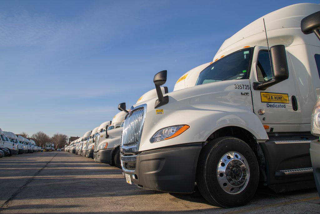 A line of J.B. Hunt Dedicated Contract Services trucks parked in a truck yard.